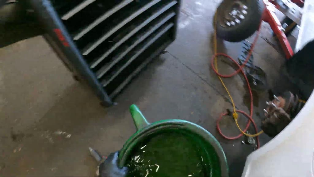 The mechanic lifted the filled green drain pan and carried it through the shelving aisle to the waste-fluid tank. The pa