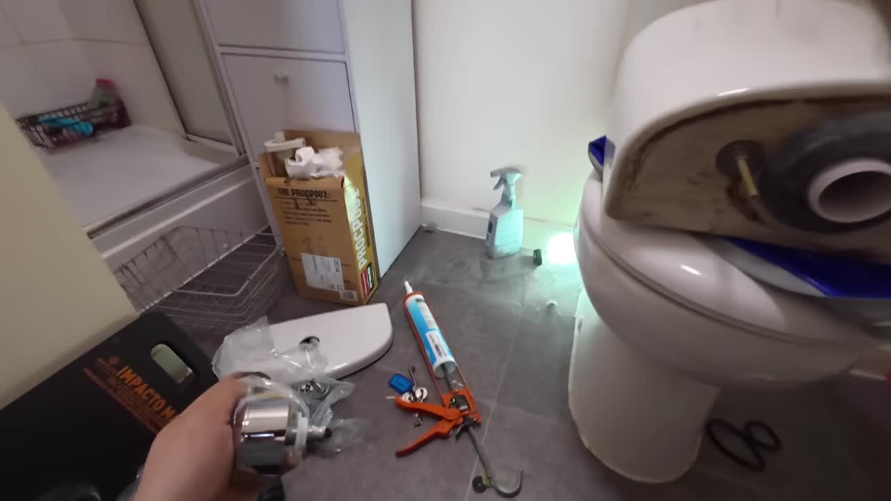 Step keyframe: the toilet tank on the floor with the new siphon parts staged beside it